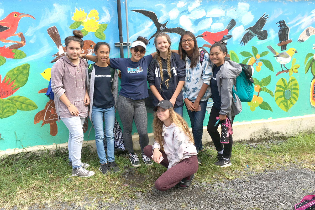 Grade 8 students standing in front of mural of Hawaiian forest birds on Big Island