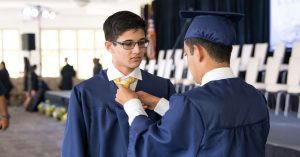 Student helping a classmate tie his tie at commencement