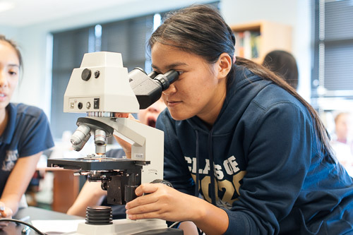 Female high school student looking through a microscope