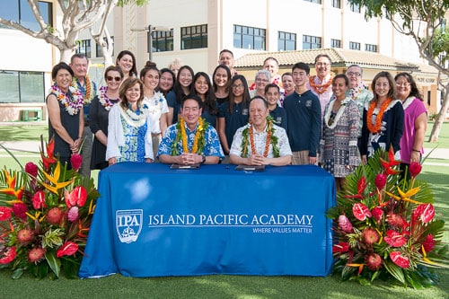 Heads of School for Kamehameha and Island Pacific Academy signing document with students behind them.