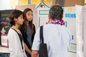 Students explaining research project to science fair judge
