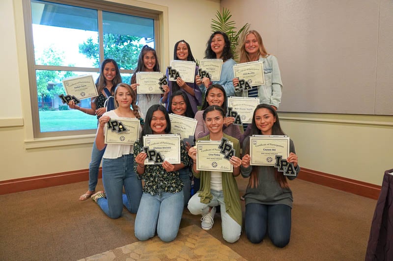 Girlsʻ varsity volleyball team showing off their certificates.