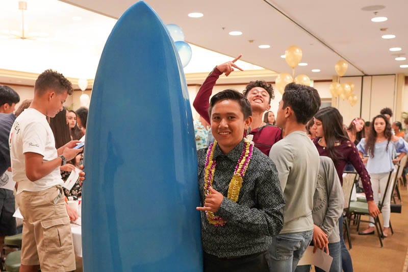 Student stands next to surfboard prize