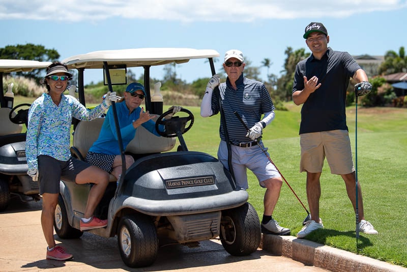 Foursome poses for photo in front of golf cart