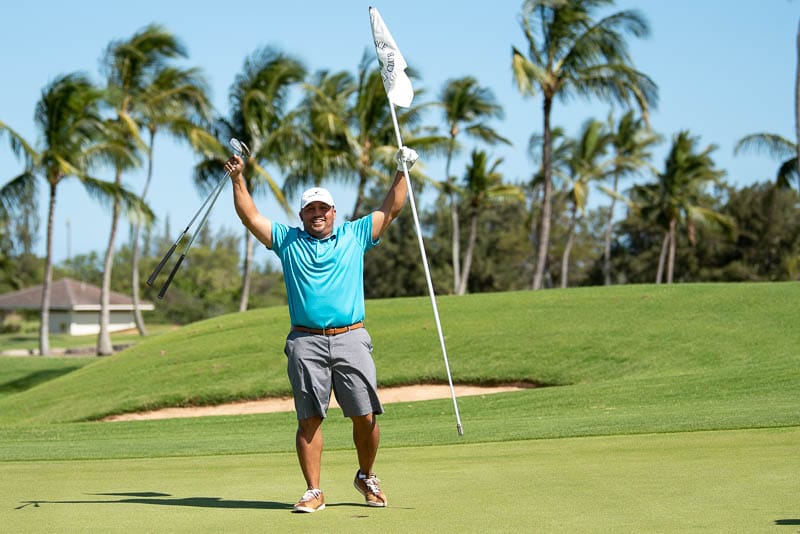 Golfer holds pin and clubs above his head in celebration