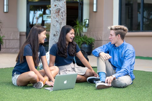 Three high school students sitting on the grass talking