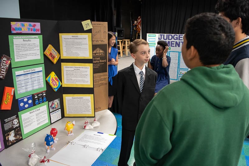 Student standing in front of science fair project talking to judge.