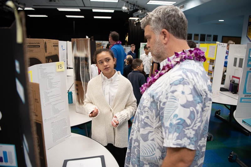 Student standing in front of science fair project talking to judge.