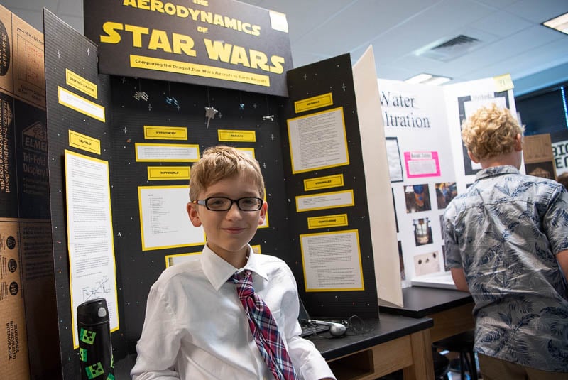 Student standing in front of science fair project talking to judge.