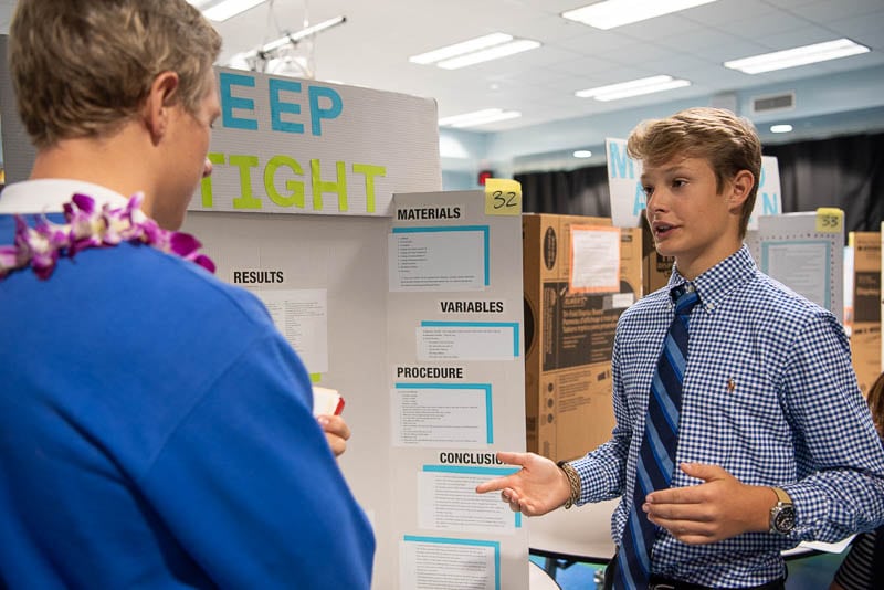 Student standing in front of science fair project talking to judge.