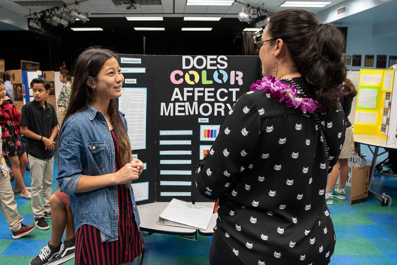 Student standing in front of science fair project talking to judge.