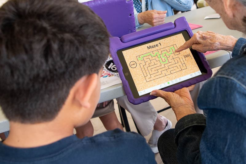 Student and a senior play a maze game on an iPad