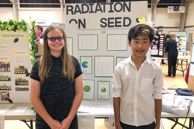 iddle school students standing in front of science fair project