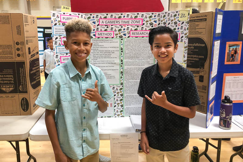 iddle school students standing in front of science fair project