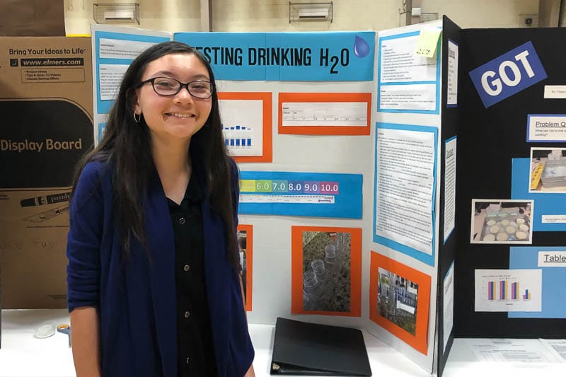 iddle school student standing in front of science fair project