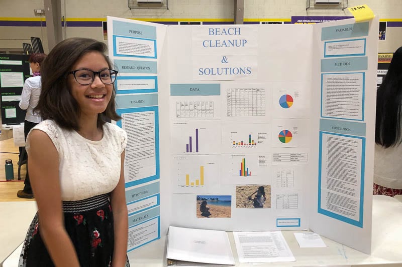 iddle school student standing in front of science fair project