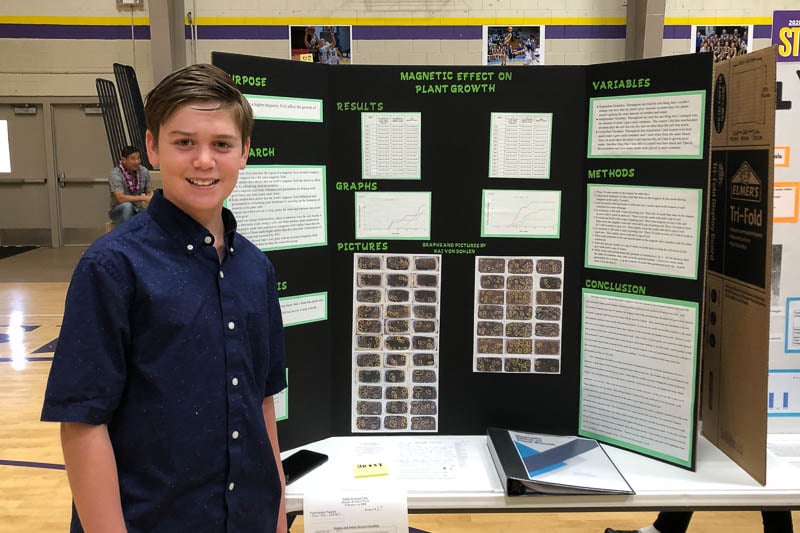 iddle school student standing in front of science fair project