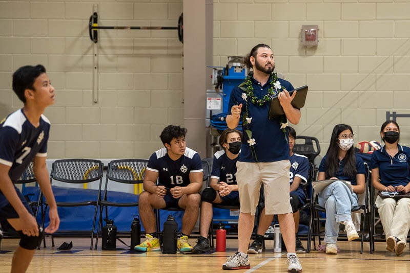 Coach watching volleyball team from sidelines.