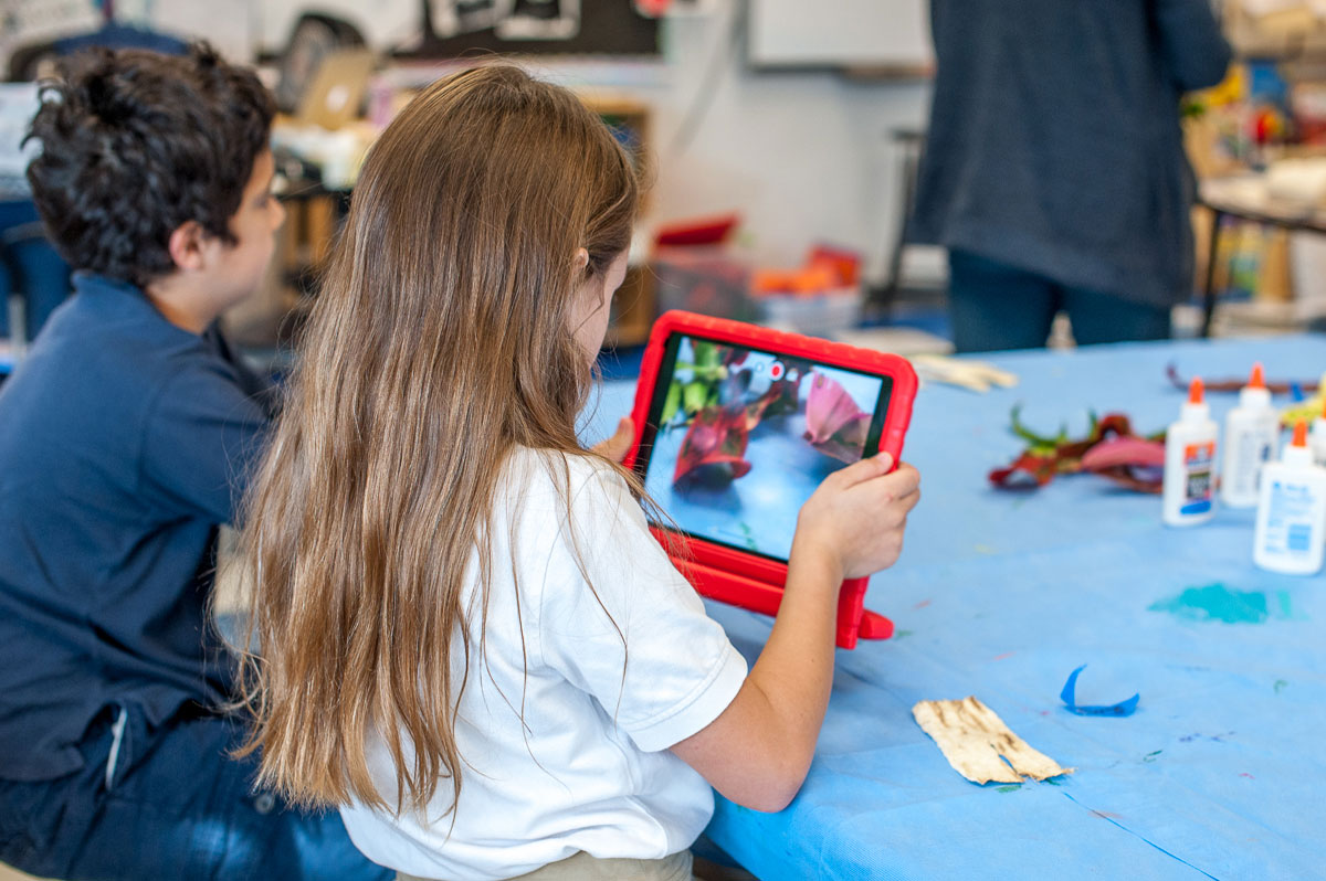 IPA students at a table with 1 student holding an ipad device